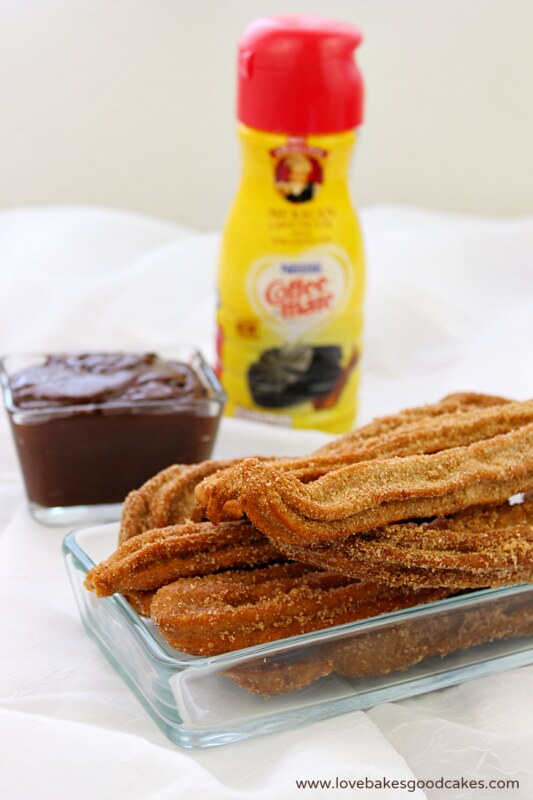 Mexican Chocolate Churros with Dipping Sauce in a clear dish with dipping sauce and a bottle of coffee mate.
