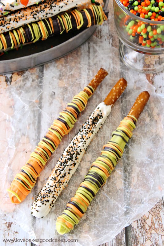 Candy Dipped Pretzel Rods laying on parchment paper with candy pieces.