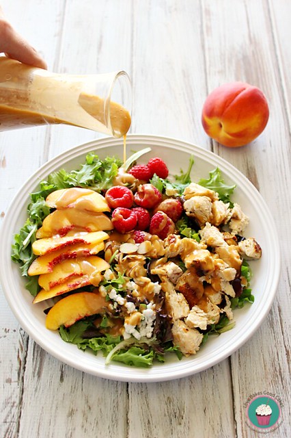 Peach & Raspberry Chicken Salad with Peach Vinaigrette in a bowl with dressing being poured over the top.