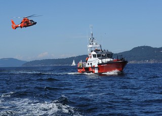 An MH-65 Dolphin helicopter aircrew from U.S. Coast Guard Air Station Port Angeles, Wash., makes an approach toward Canadian Coast Guard Ship Cape Naden, a 47-foot motor lifeboat from Sidney, British Columbia, during a training exercise in Moresby Passage, Aug. 7, 2014. The U.S. Coast Guard and Canadian Coast Guard crews organized the training event to practice skills necessary for safely completing a joint rescue along the international maritime border. U.S. Coast Guard photo by Petty Officer 3rd Class Katelyn Shearer.