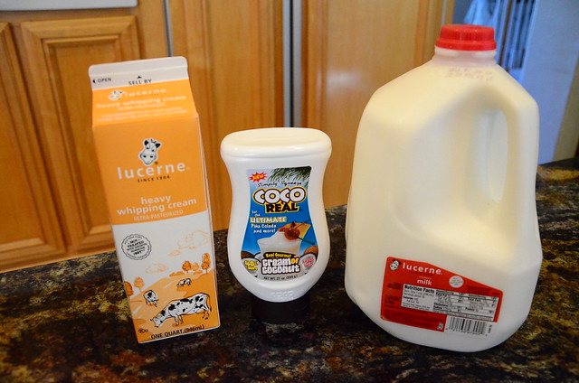 Whole milk, heavy cream, and a bottle of cream of coconut arranged on a counter.