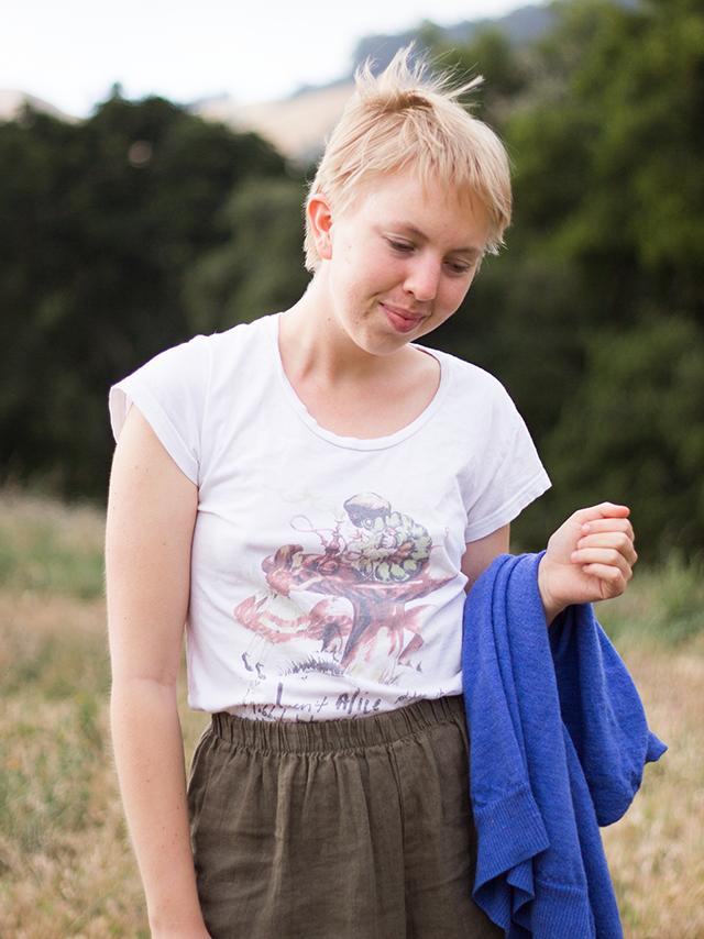 white Alice in Wonderland t-shirt, brown linen trousers, forest setting