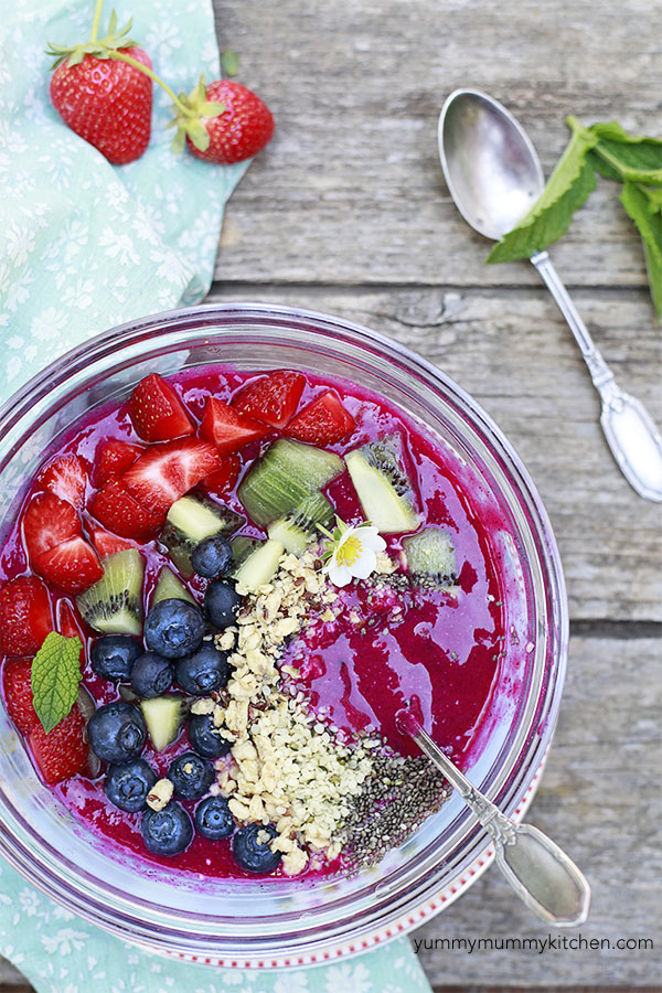 A pink dragon fruit smoothie bowl topped with blueberries, strawberries, kiwi, granola, and chia seeds from above. 