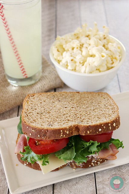 Classic Ham Sandwich on plate with a bowl of popcorn and a glass of lemonade.