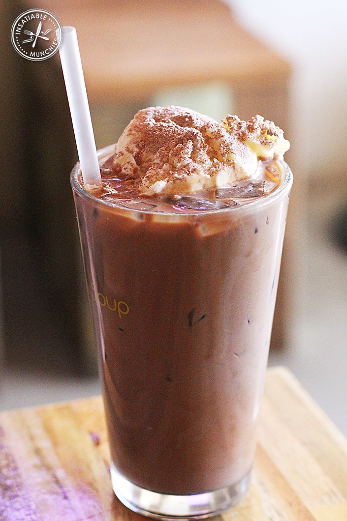 Iced Chocolate from this cafe is served in a tall glass, topped with whipped cream and a sprinkle of cocoa powder