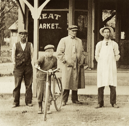 people usa signs man men history boys sepia kids buildings advertising children clothing shoes hats indiana streetscene bicycles transportation porch shops pedestrians storefronts businesses realphoto hoosierrecollections