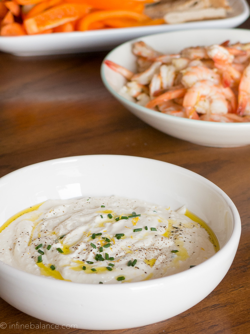 creamy feta dip in a white bowl with olive oil, cooked shrimp and toasted pita for dipping