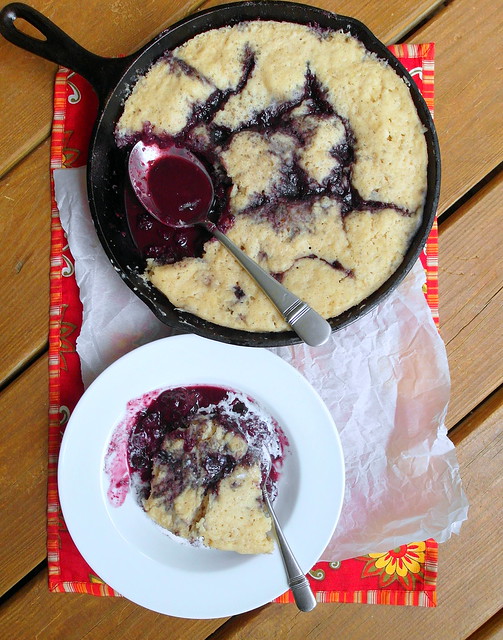Mixed Cherry-Berry Grunt in a cast iron pan with a single serving next to it in a white shallow bowl.