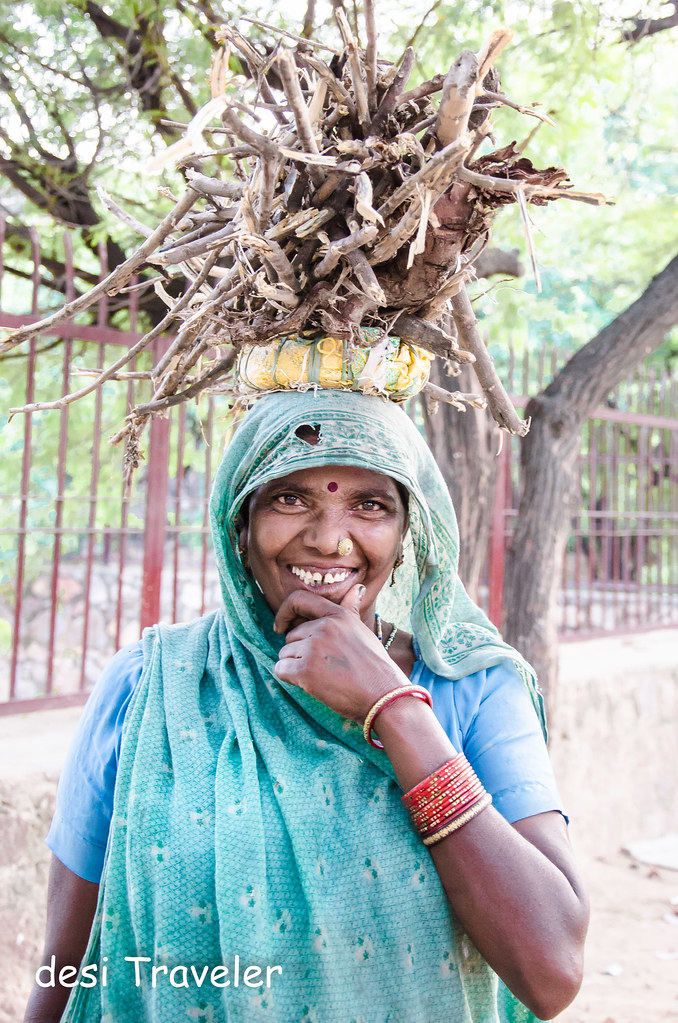 smiling woman wearing bangles with fire wood on her head