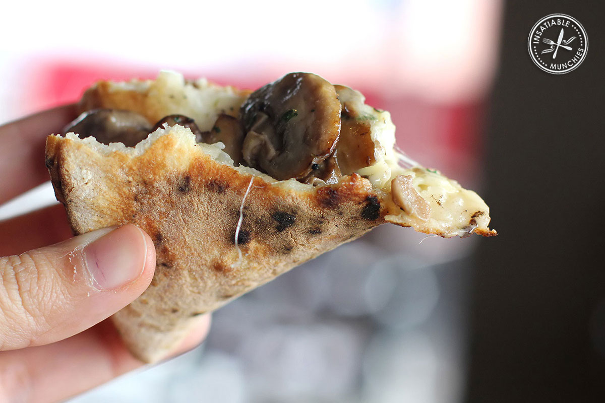 A slice of Mushroom Napolitana Pizza gets folded in half, to show that the soft fluffy base doesn't crack.
