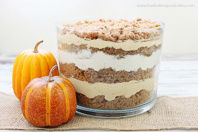 Pumpkin Spice Trifle in a clear bowl with two pumpkins near by.