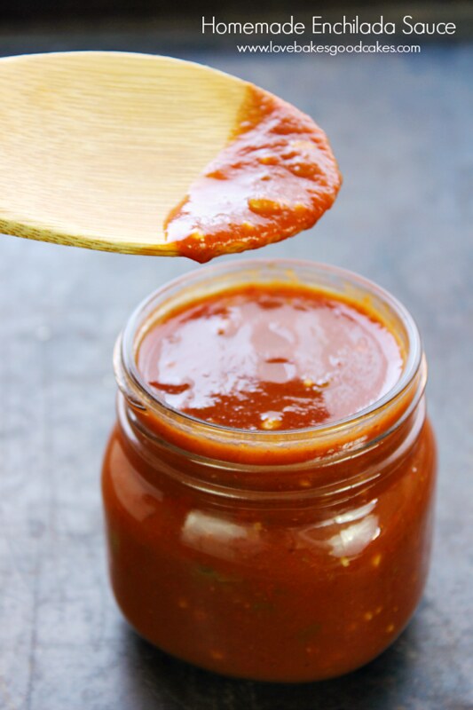 Homemade Enchilada Sauce in a glass jar with a spoon dipping into the sauce.