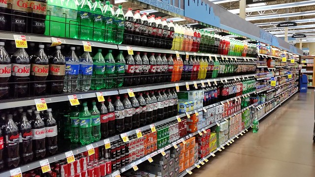 A grocery store isle with soft drink products on the shelves.