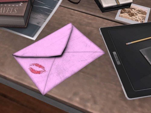 Image Description: Pink letter with a kiss on the corner on a desk with several other items.
